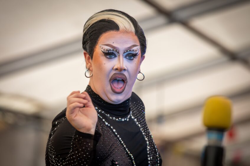 Performer with dramatic makeup and rhinestone outfit gestures mid-performance at Fife Pride 2025 under a marquee stage.
