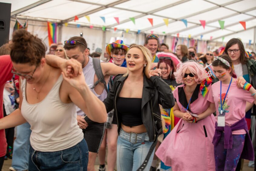 Group of people dancing inside a colourful marquee at Fife Pride 2025, wearing rainbow accessories and pride-themed outfits.