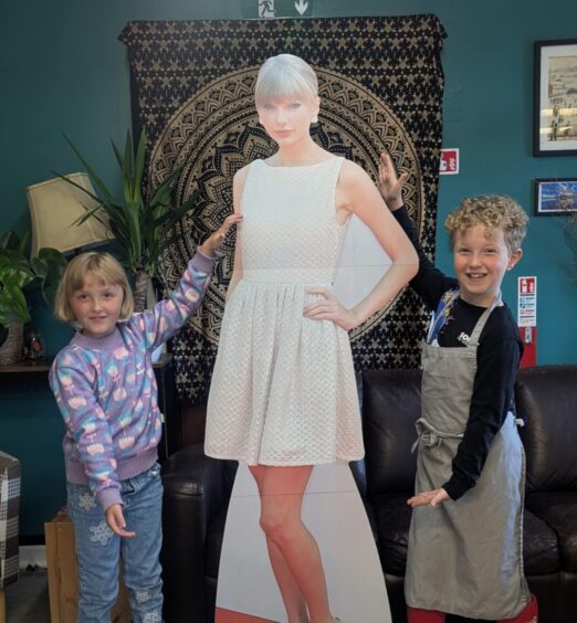 Two small children smiling beside life-sized cut-out of Taylor Swift
