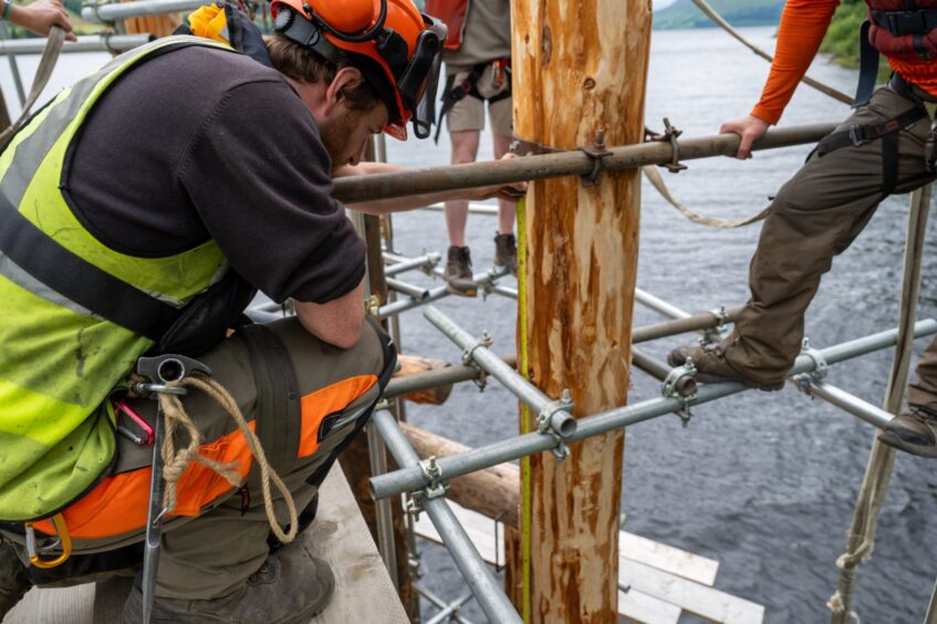 Man kneeling with measuring tape against wooden post in water