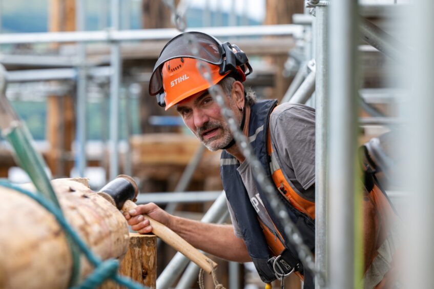 Chas Heath in hard hat holding mallet as he moves large piece of timber into place