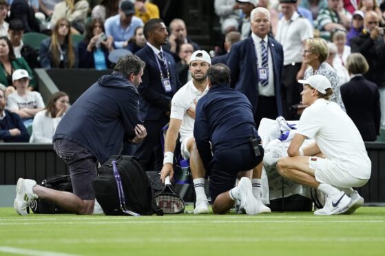 Grigor Dimitrov (centre) reacts as he receives treatment for an injury during his Gentlemen's Singles match against Jannik Sinner (right) on day eight of the 2025 Wimbledon Championships at the All England Lawn Tennis and Croquet Club, London. Picture date: Monday July 7, 2025.