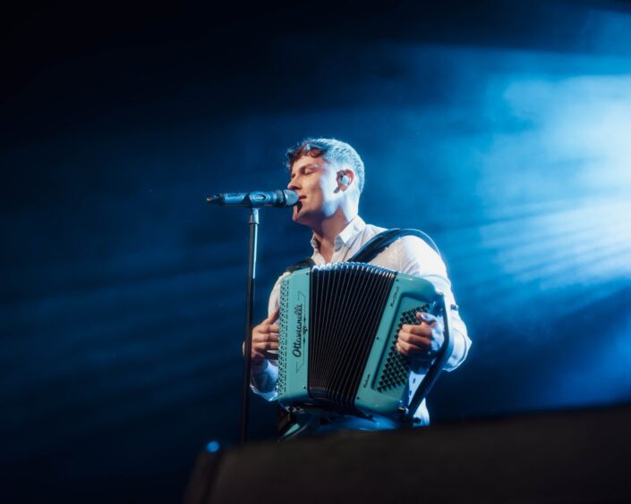 Man singing into microphone on stage while playing accordion