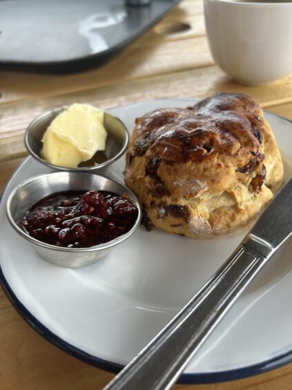 A fruit scone served on a plate with jam and butter.