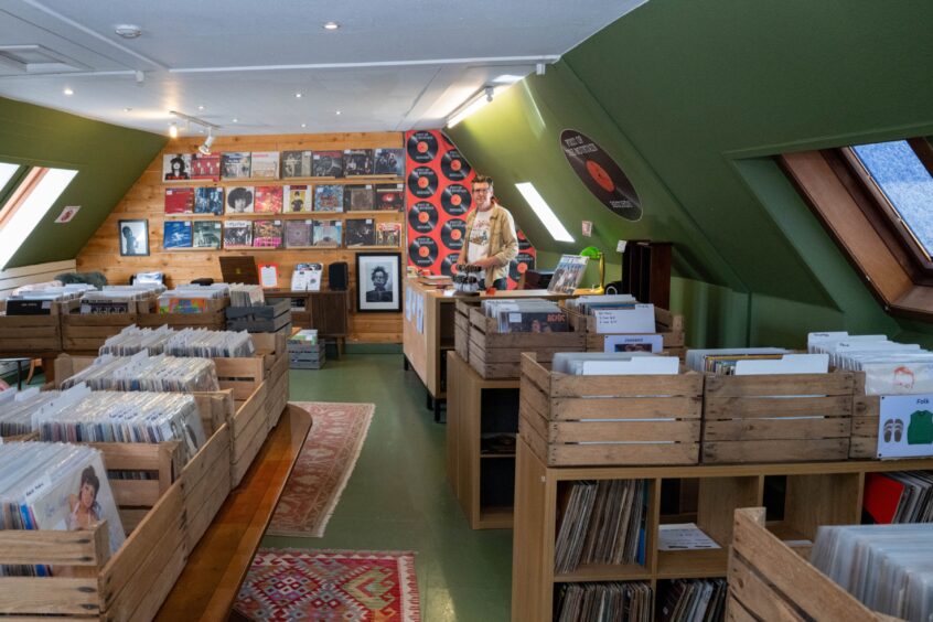 Colin Tennant in small, sloping ceilinged, oilve green-painted room, with records set out in crates on tables