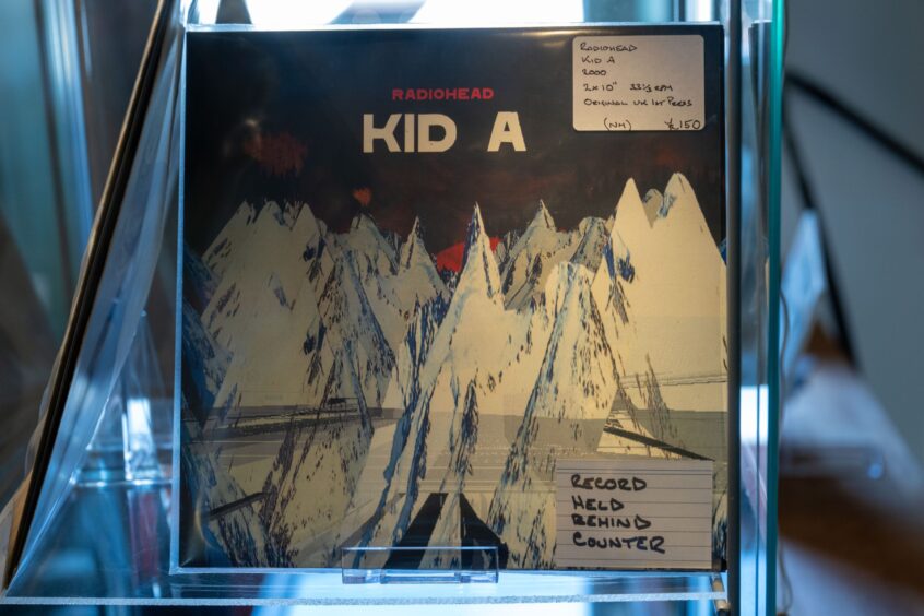 Copy of album Kid A inside display case with stiicker saying 'record held behind counter'