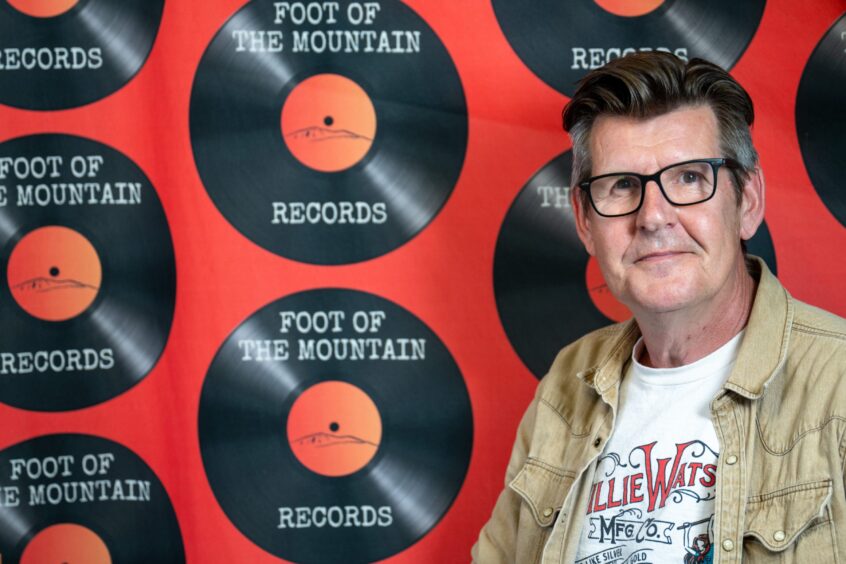 Colin Tennant in front of wall with Foot of the Mountain Record logo - a record with shop's name written on it
