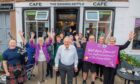 Dennis Arnold celebrates completing a walking challenge with supporters including piper Lacey Colville outside The Singing Kettle Cafe in Alyth.