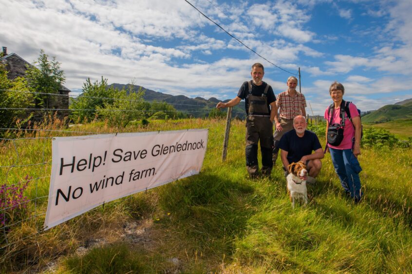 Group of people beside sign on fence which says 'Help! Save Glen Lednock. No wind farm' and mountains behind