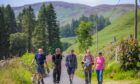 Five people walking on narrow road surrounded by mountains and trees