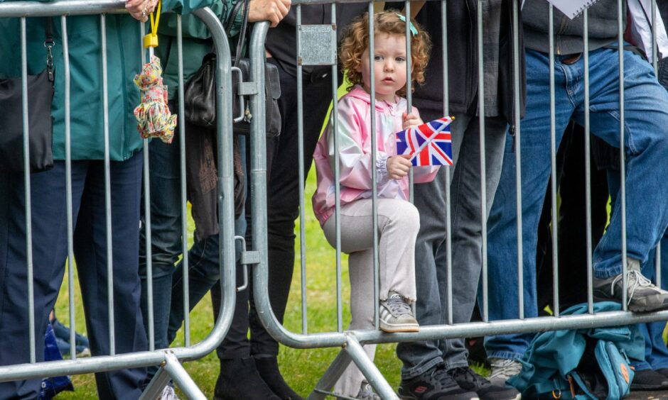 A little girl with a Union flag waits behind a fence