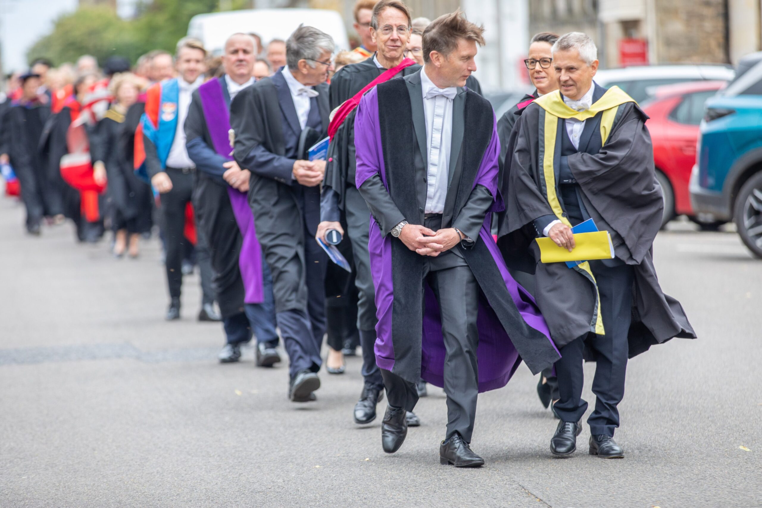 A procession of academic staff in ceremonial robes walk down the street during the St Andrews University graduation parade, heading from Younger Hall to St Salvator’s Quad.