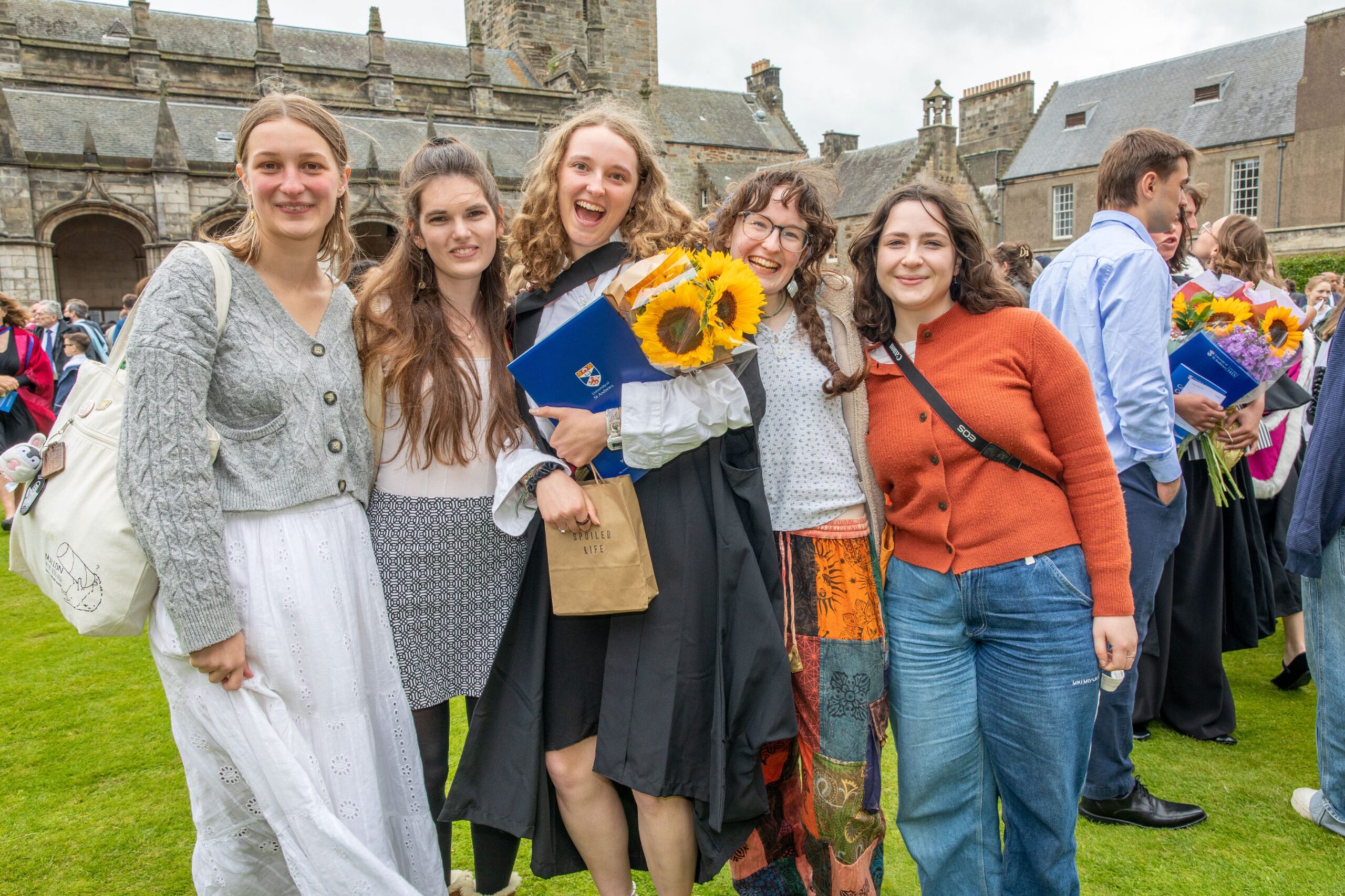 Graduate Emelia Brooke holding sunflowers and a folder, smiling with a group of friends in St Salvator’s Quad after Friday’s graduation ceremony.