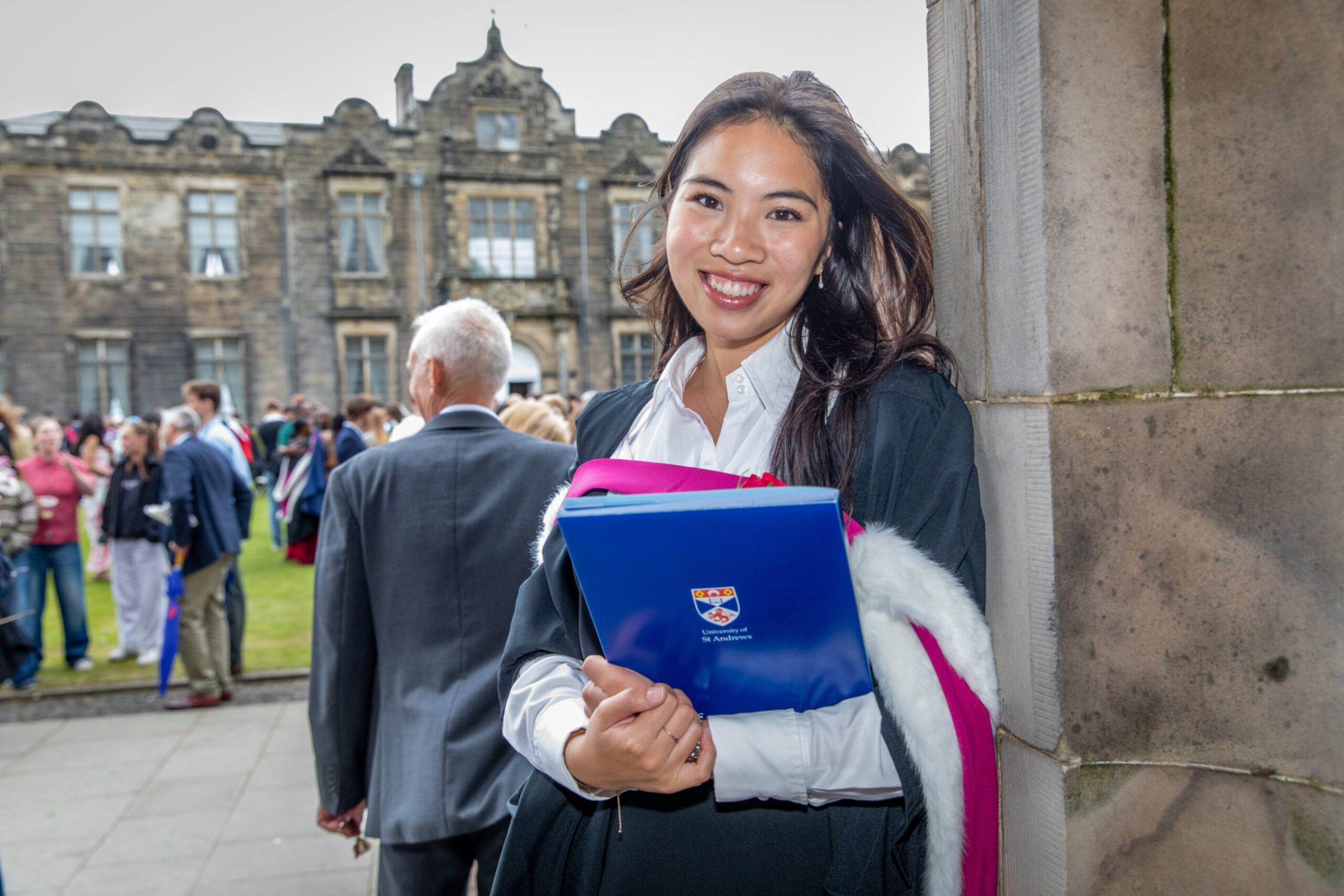 raduate Sarah Ng from Yorkshire smiling in academic robes and holding her certificate folder at St Andrews graduation.