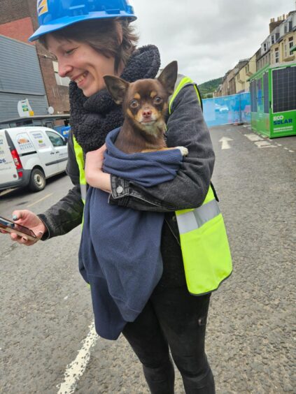 Vilo, wrapped in a blue jumper, with Katie McCandless from Missing Pets Perth and Kinross, who is wearing a safety hat and high-viz vest