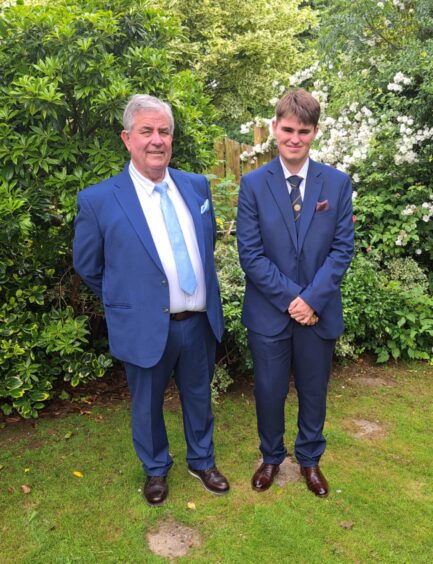 Frazer Hutchison, senior and junior, in smart suits in front of shrubbery