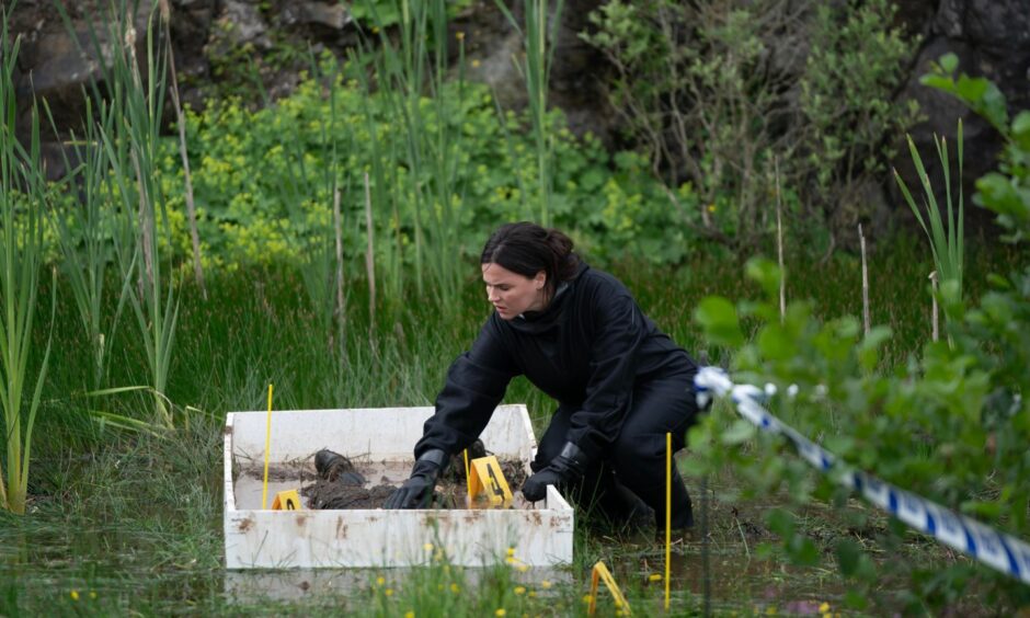 An actress plays the role of forensics expert in Karen Pirie. She is examining a body outside.