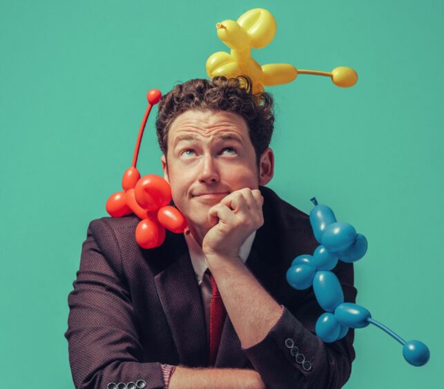 Magic Gareth with three colourful balloon dogs on his head and shoulders. Balloonatic show preview for Fife July What's On.