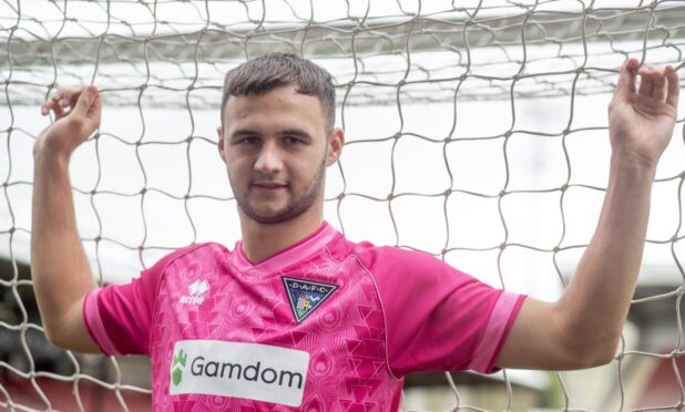 Dunfermline Athletic loan signing Mason Munn stands with his fingers through the goal nets.