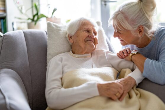 Woman in 50s leaning in supportively to seated woman in 80s.