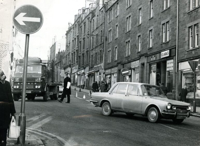a policeman stands in the road during a traffic hold up on a Hilltown street in 1973.