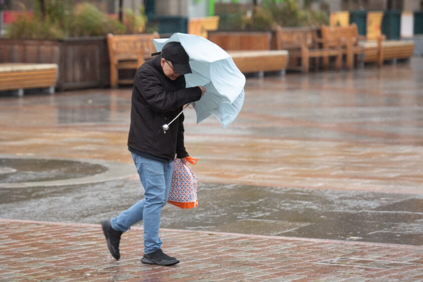 A man struggles to hold his umbrella amid heavy winds.