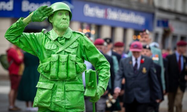 Entertainer dressed as a green Toy Soldier with helmet, utility vest and prop metal detector salutes during the City of Perth Salute 2025 parade.