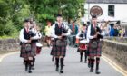 Doune Pipe Band in traditional dress playing bagpipes while marching over the Bridge of Dochart at Killin Highland Games 2025.