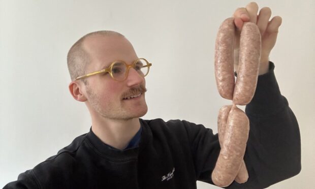 Jacob Smith holding four raw sausages.