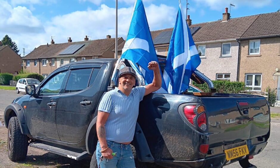 Protest organiser David Tarbett raises his fist as he stands in front of a pick-up truck which has two Saltire flags flying from it