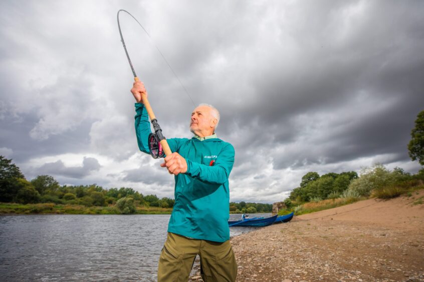 Milos Vasiljevic fishing on River Tay with small boat and dark clouds behind him