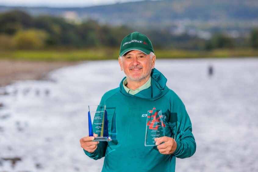 Milos Vasiljevic holding two glass trophies with River Tay behind