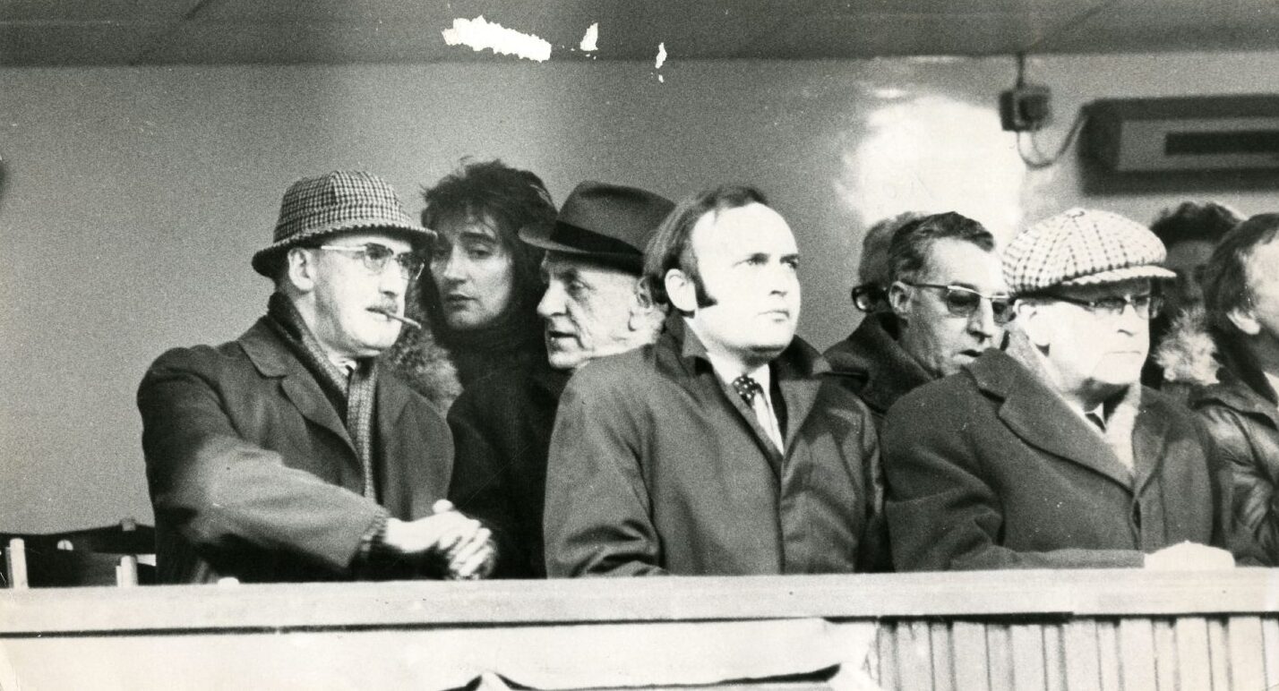 Rod Stewart at Tannadice to watch Celtic play United in 1977. The singer is among a group of men wearing hats, scarfs and overcoats on what looks like a chilly day.
