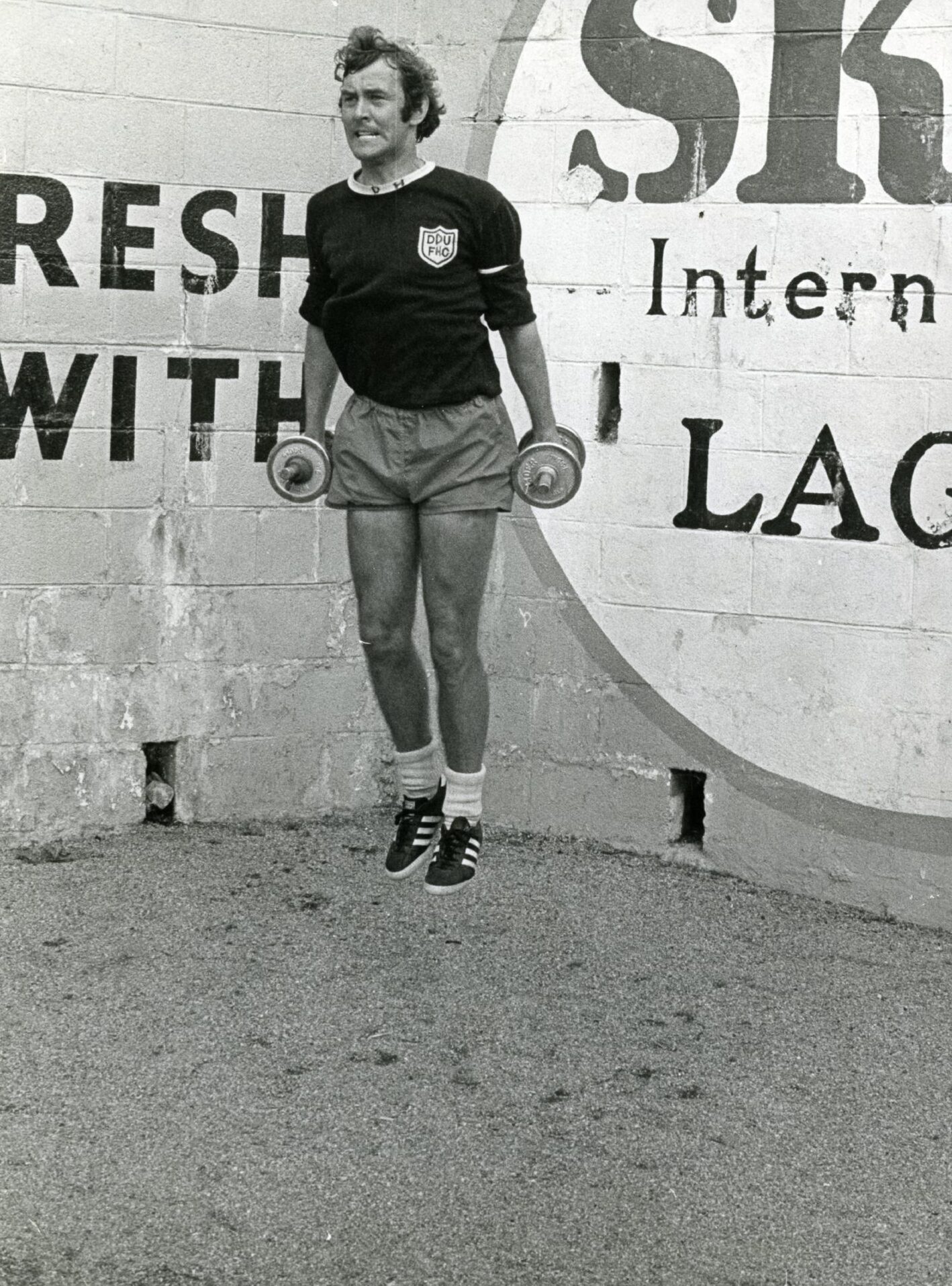 Doug Houston wears a Dundee United training top and shorts as he jumps in the air while holding a dumbbell in each hand.