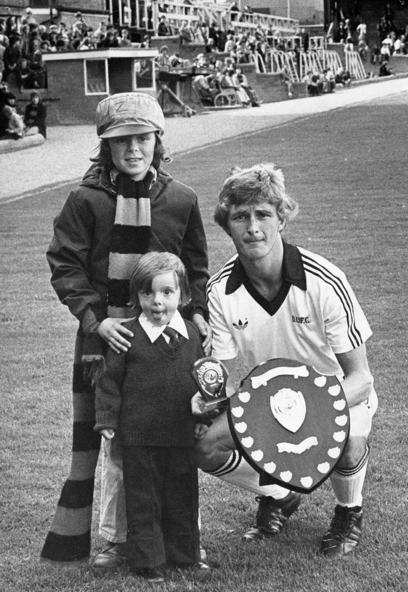 Defender Paul Hegarty holds a large shield presented to him as player of the month. He is with the two young fans who handed it over.