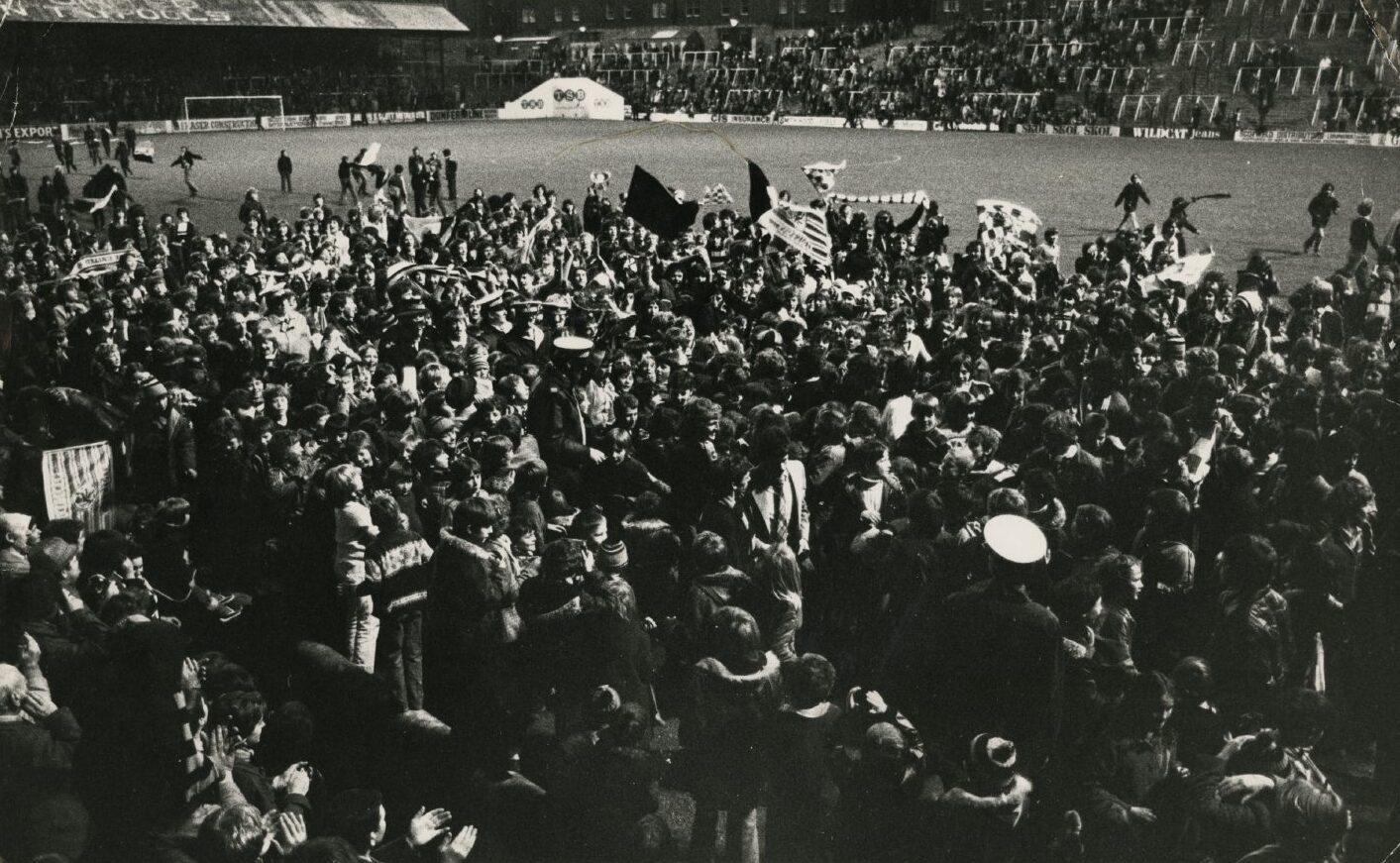 A large crowd of people on the pitch at a gala day celebrating United's League Cup win over Aberdeen. Some are waving scarfs and flags.