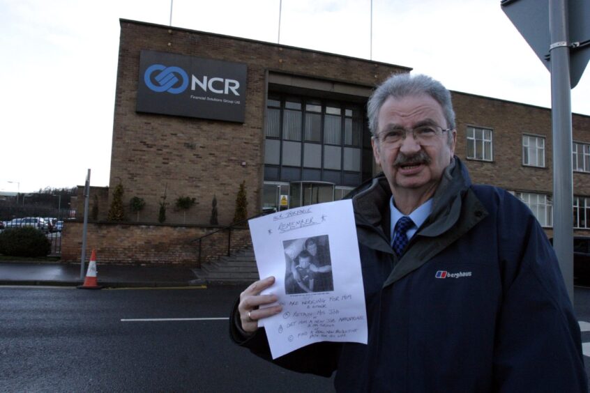 Rev Erik Cramb holds a poster as he stands outside the NCR factory in Dundee.