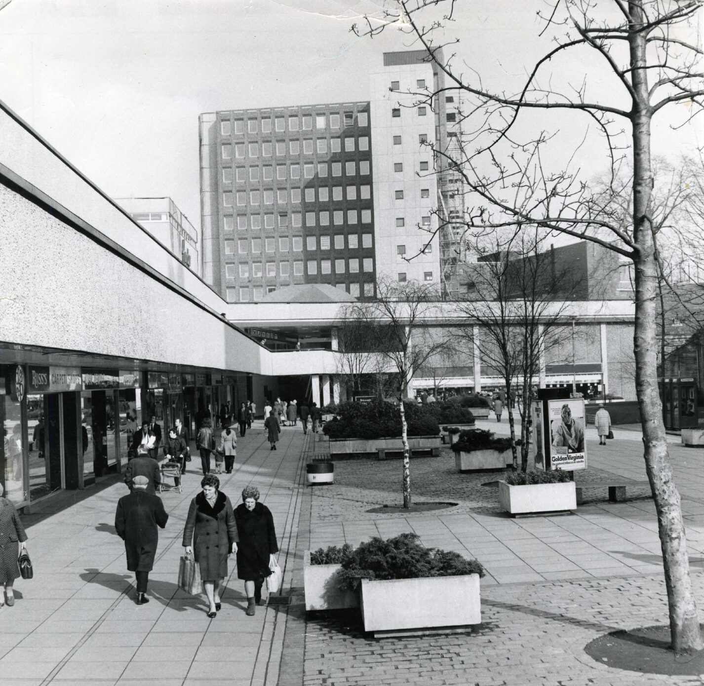 Shoppers with bags walk along past shops.