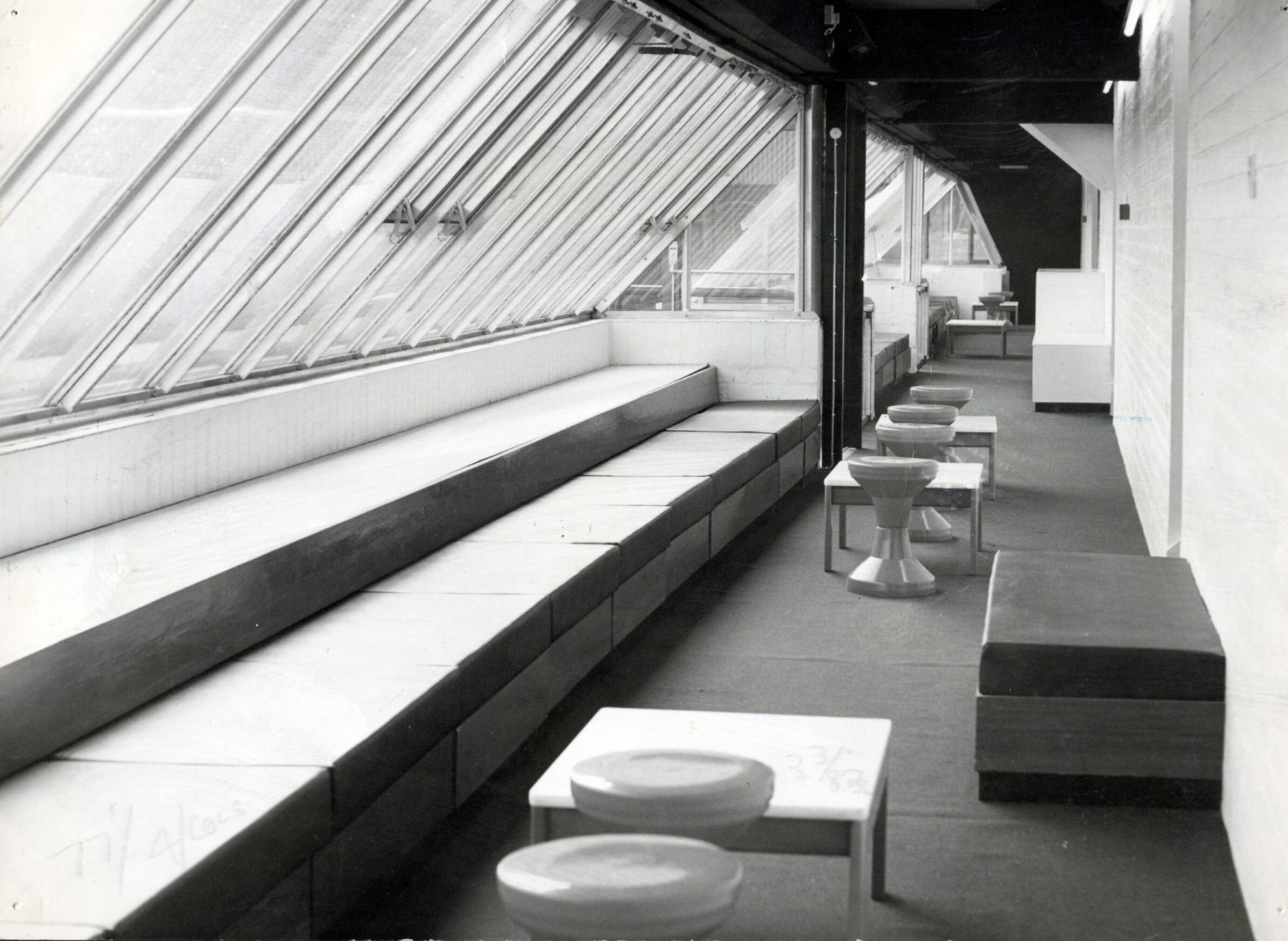 The lounge below the grandstand at Tannadice, with padded seats, tables and stools and sloping glass windows looking out on to the pitch.