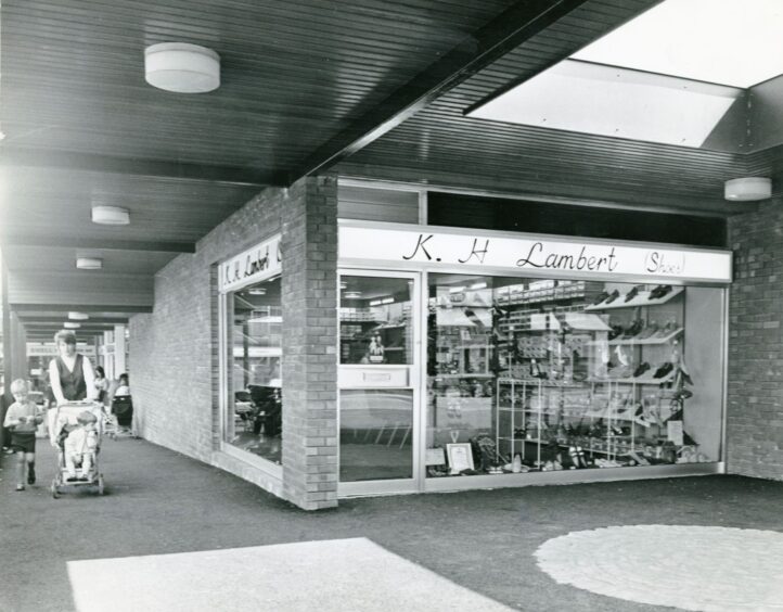 A couple walking past Lambert shoe shop with shoes in the window display.