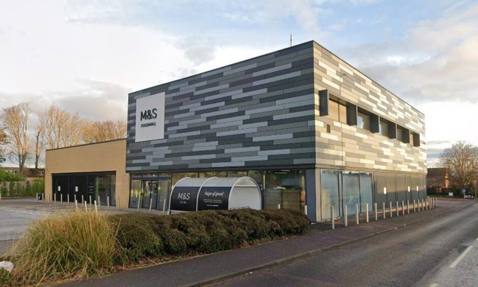 The outside of the M&S Food store in St Andrews. It's a square standalone building with glass windows at ground level and a carpark at the front.