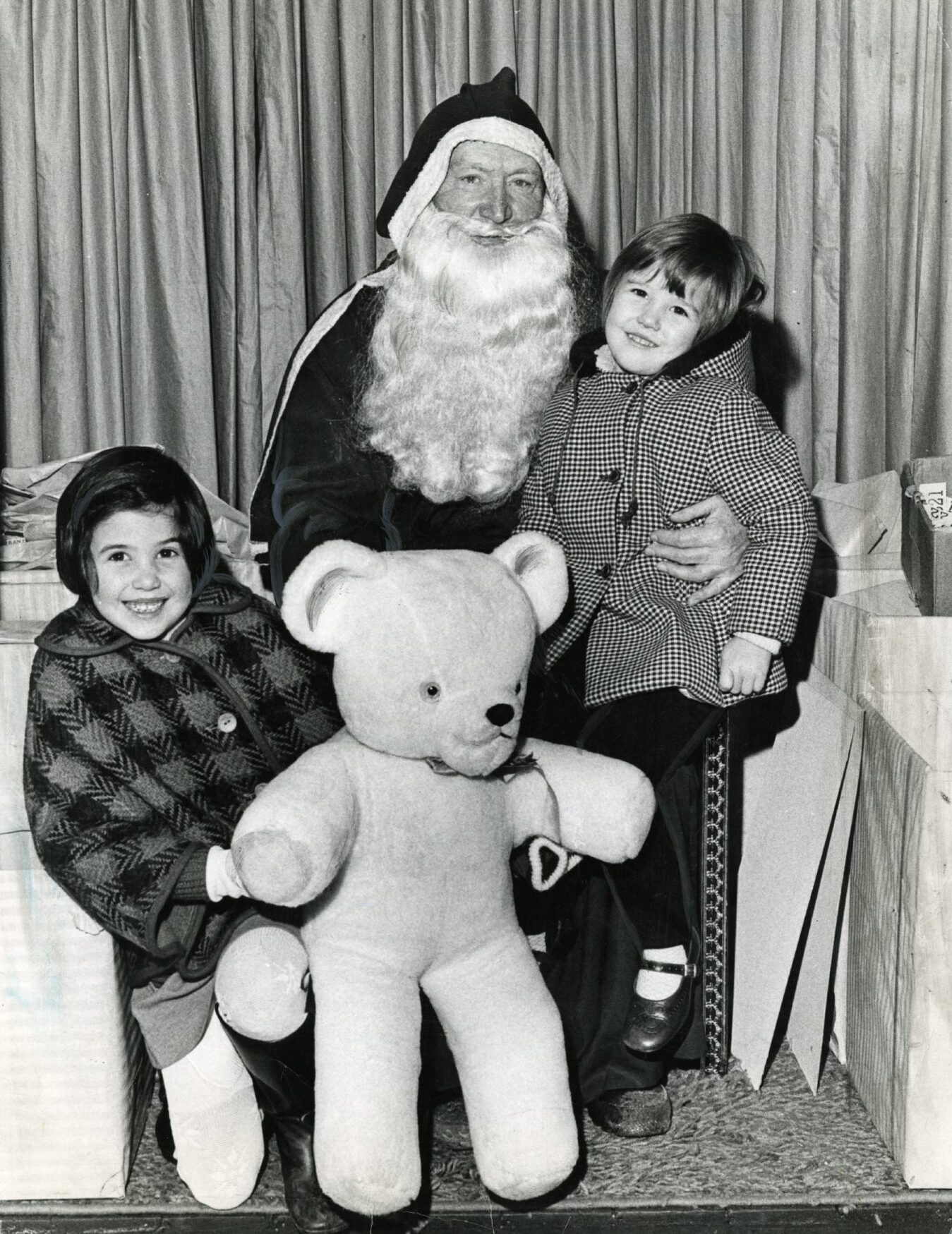 Children posing with Santa Claus, one holding a giant teddy bear. 