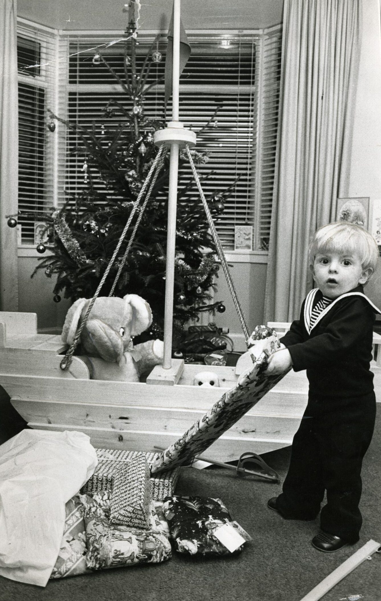 A boy unwraps Christmas present in front of the tree