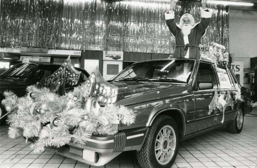 Santa emerges from the sunroof in a car in the 1980s.