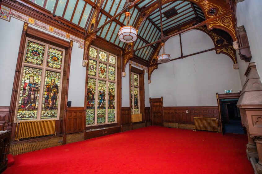 Old council chamber with tall stained glass windows, wood panelling and timber vaulted ceiling
