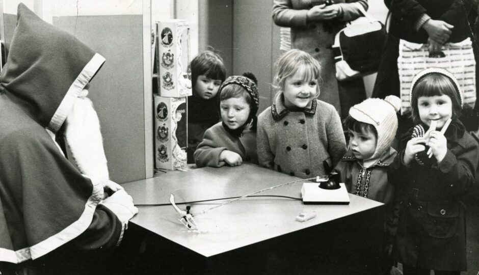 Santa with a toy helicopter, watched by a group of small children.