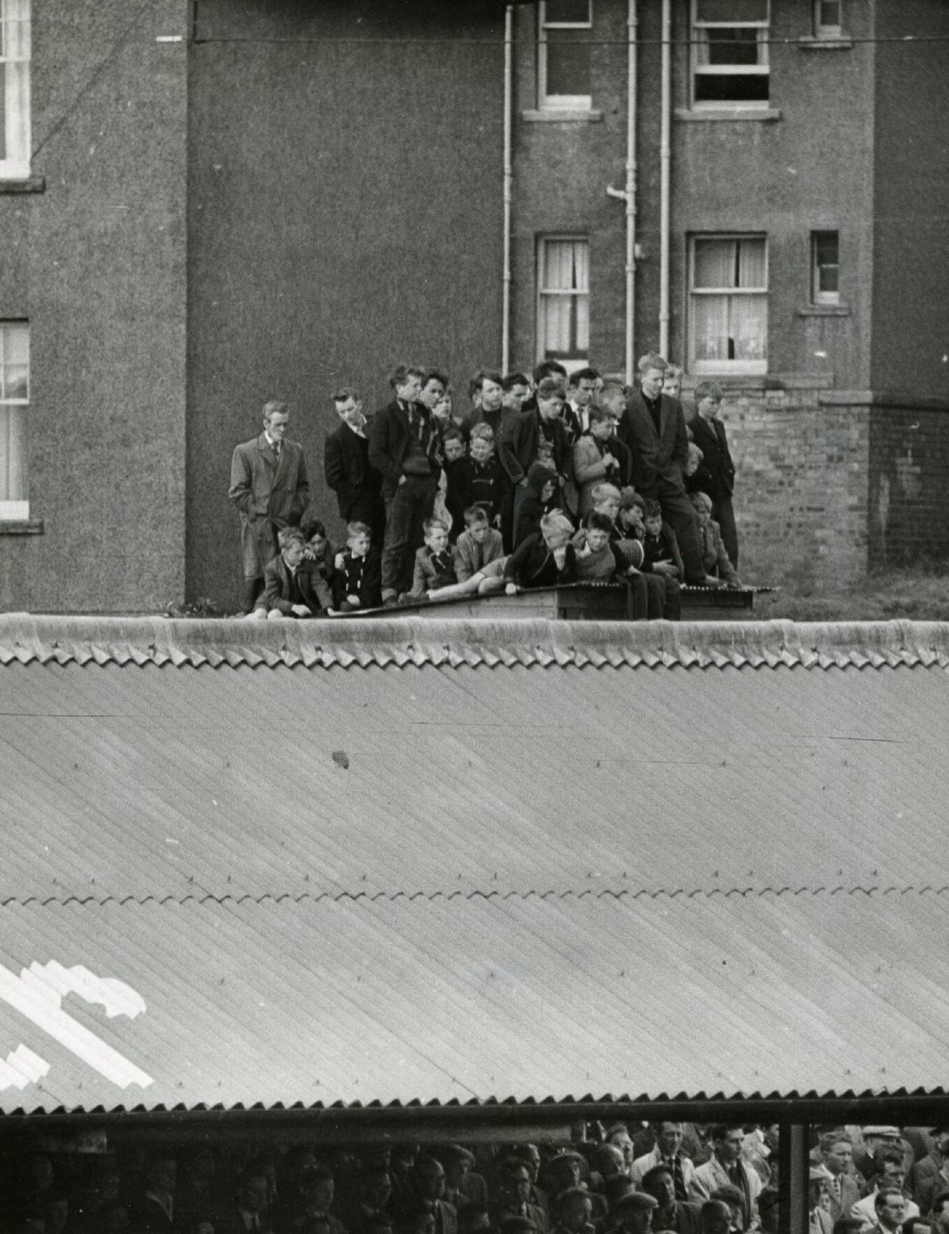 a group of people standing on a shed to see the match from outside the ground