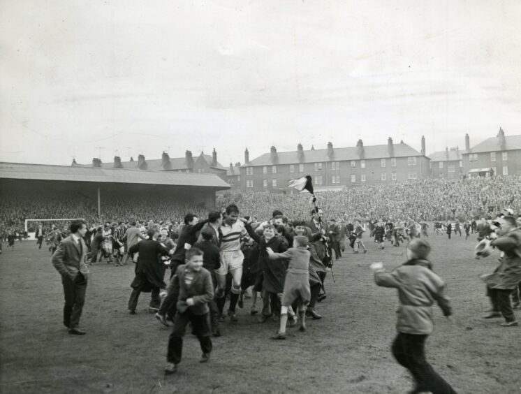 Dundee United fans surround a player on the Tannadice Park pitch.