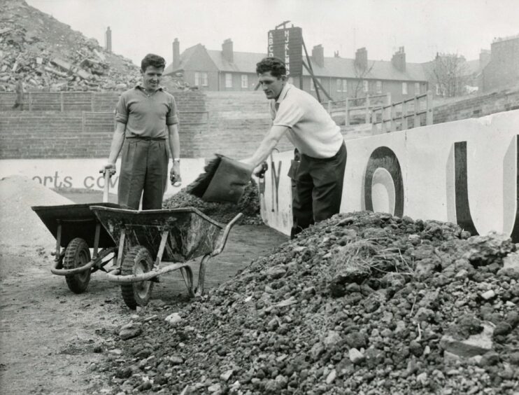 two players shovelling dirt into wheelbarrows.