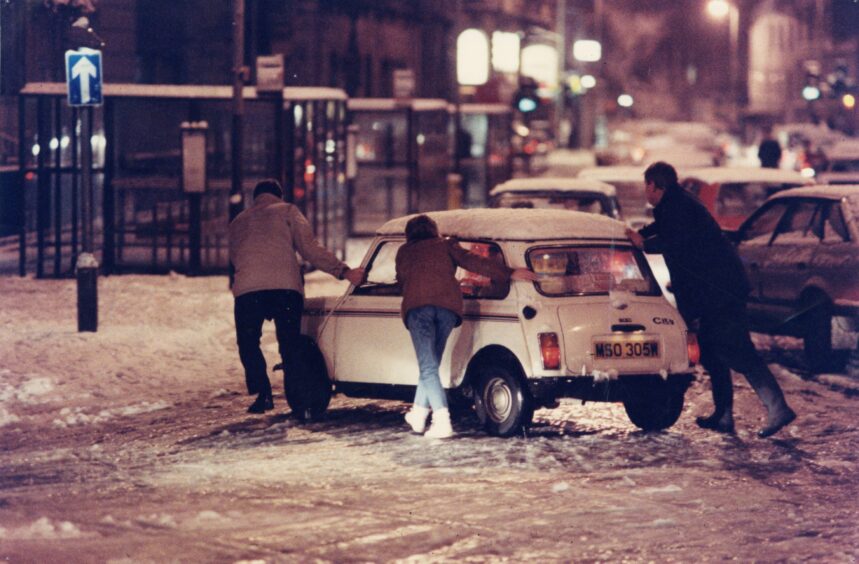 People pushing a stuck mini off the road in Albert Square. 